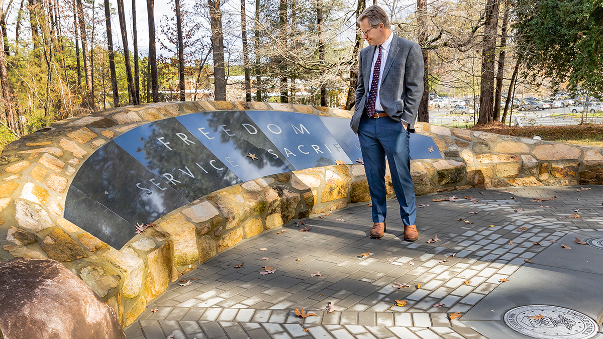 Chancellor Kevin M. Guskiewicz standing next to a veterans memorial that says 'freedom, service, sacrifice'