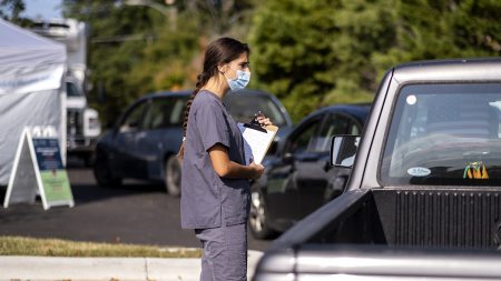 Nursing student holding a clip board beside a car.