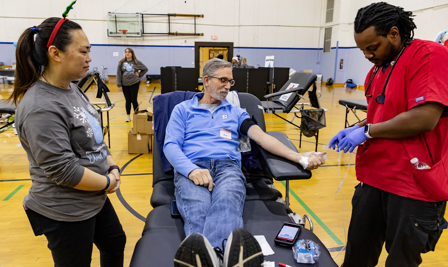 Two people stand next to a person donating blood.