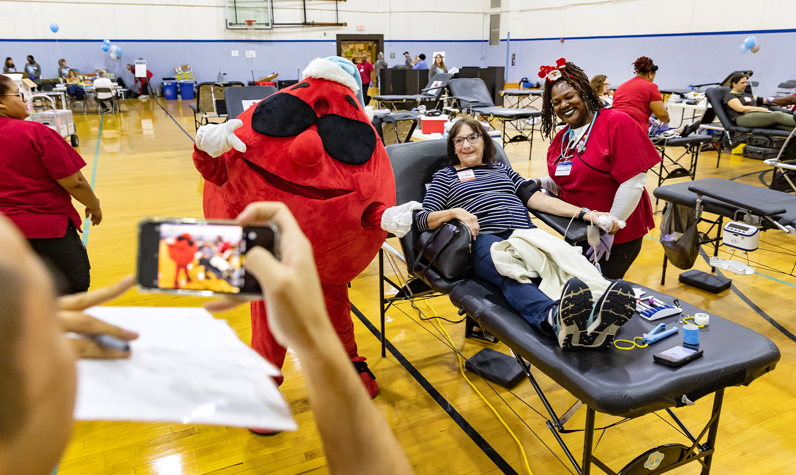 A blood mascot takes a photo with a blood donor.