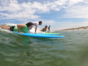 Three students lay on surfboards in the ocean