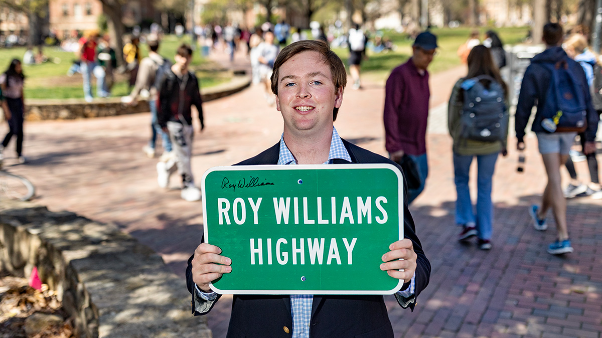 Will holding a Roy Williams Highway sign.