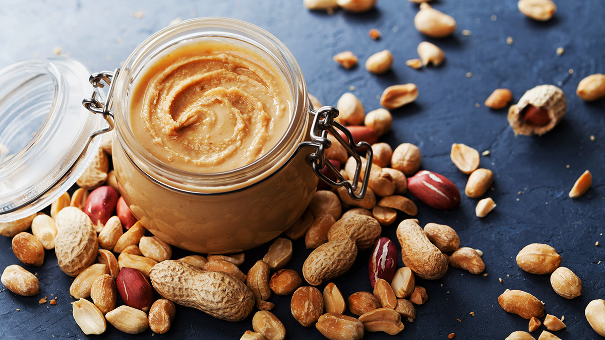 A jar of peanut butter with nuts around it.