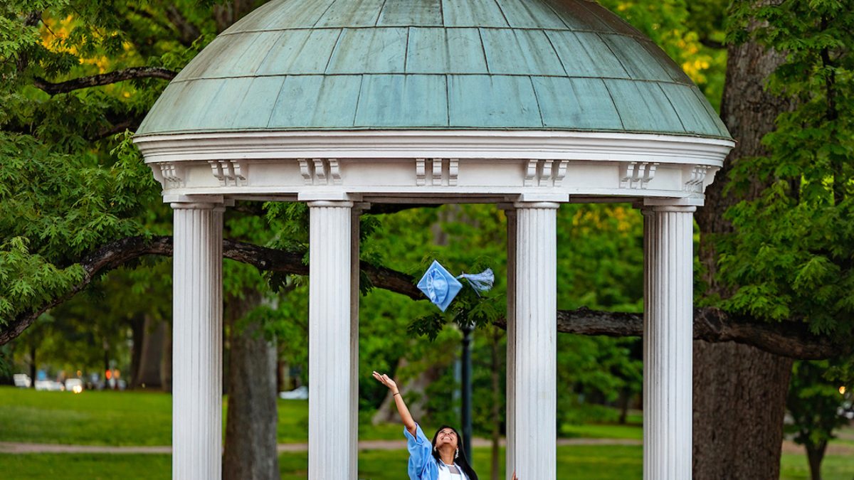 A student tosses her graduation cap into the air in front of the Old Well