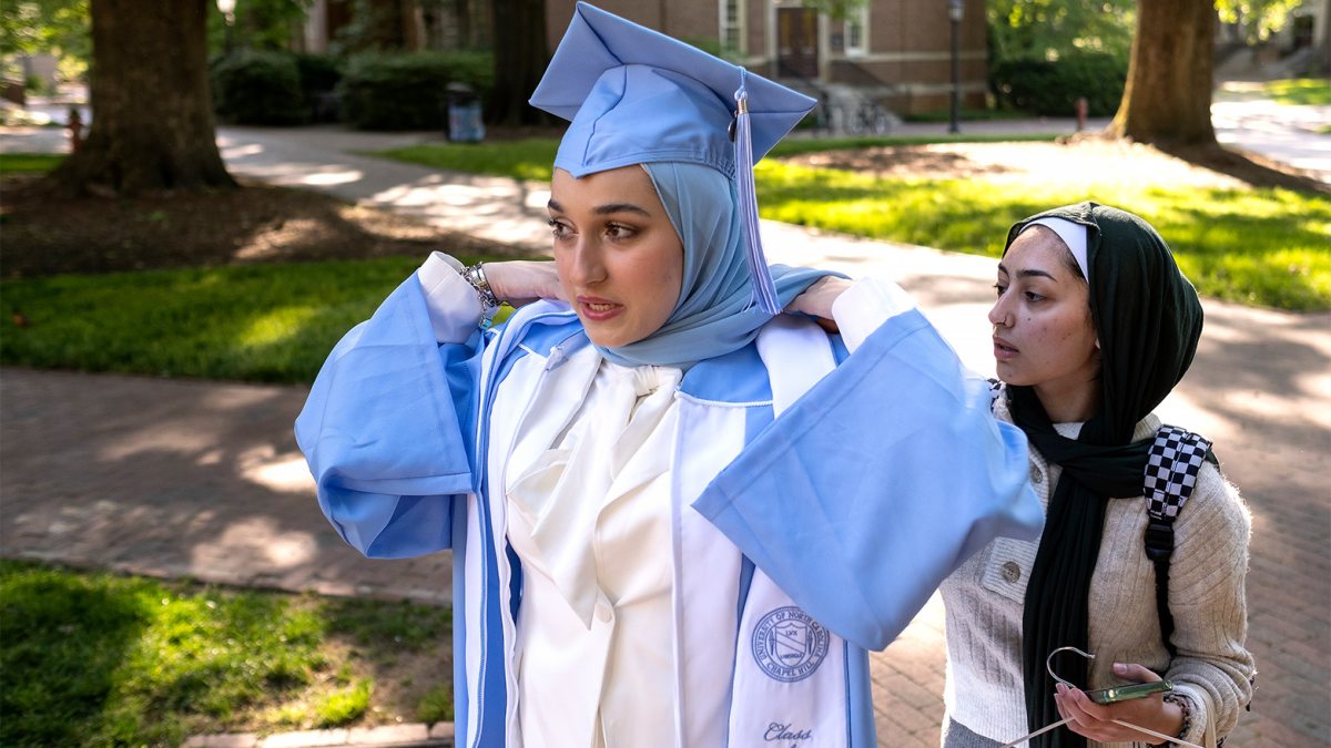 A UNC student has their graduation gown adjusted.