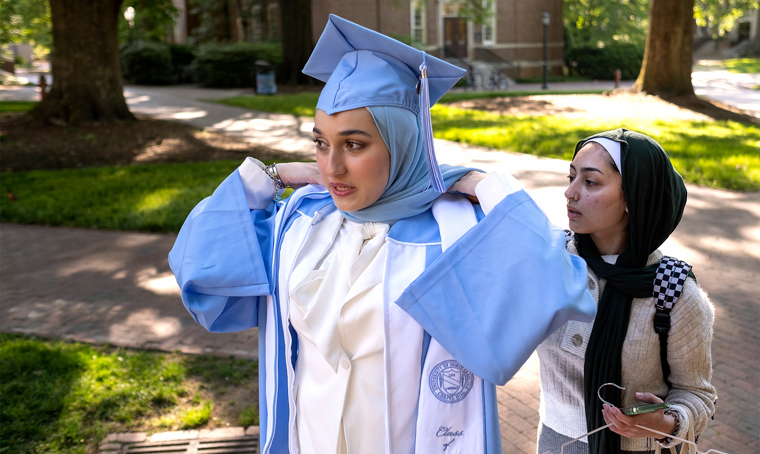 A UNC student has their graduation gown adjusted.