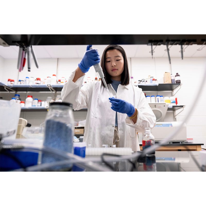 A student named Anna Jin transfers liquid from a syringe into a vial.