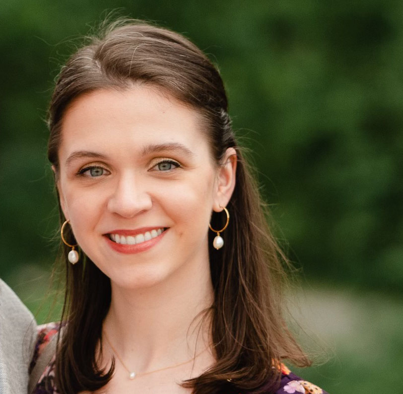Alexandra Wojda-Burlij smiles at the camera with bright green foliage in the background.