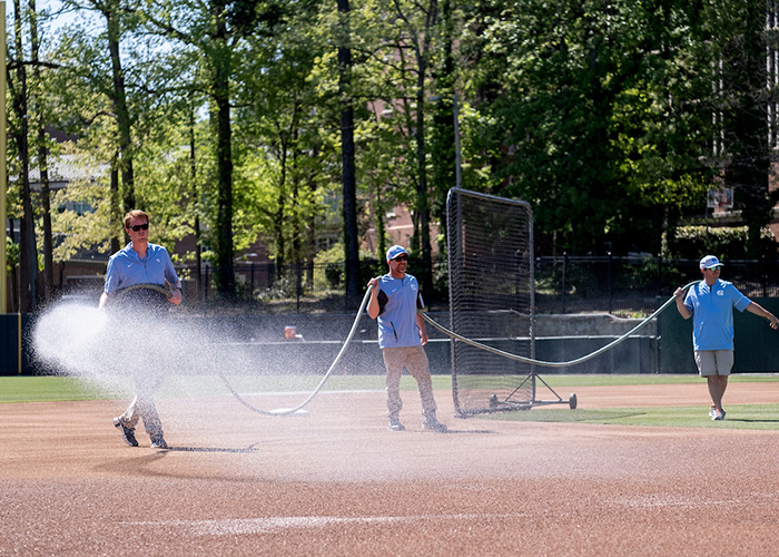 People spraying a baseball field. 