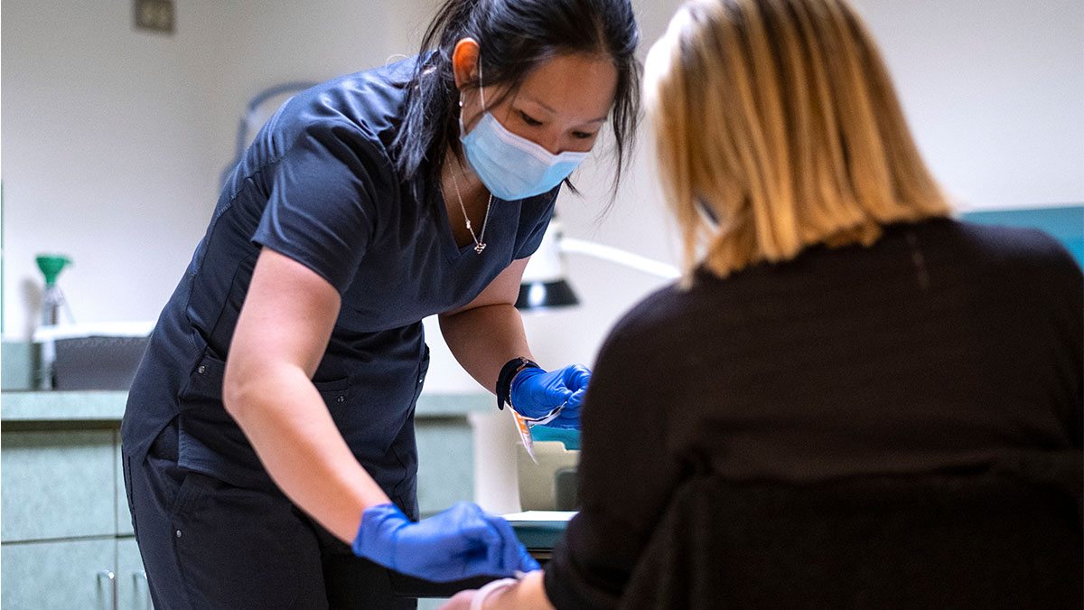 occupational health nurse Jeanne Brueggemann performs a routine mask fit test on Chelsi Holle. This was a common test at the clinic before mask-wearing became the new normal. (Jon Gardiner/UNC-Chapel Hill)|