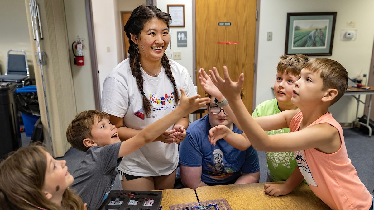 Young students try to catch a flying disk while a college student, Fiona Chen, watches them.