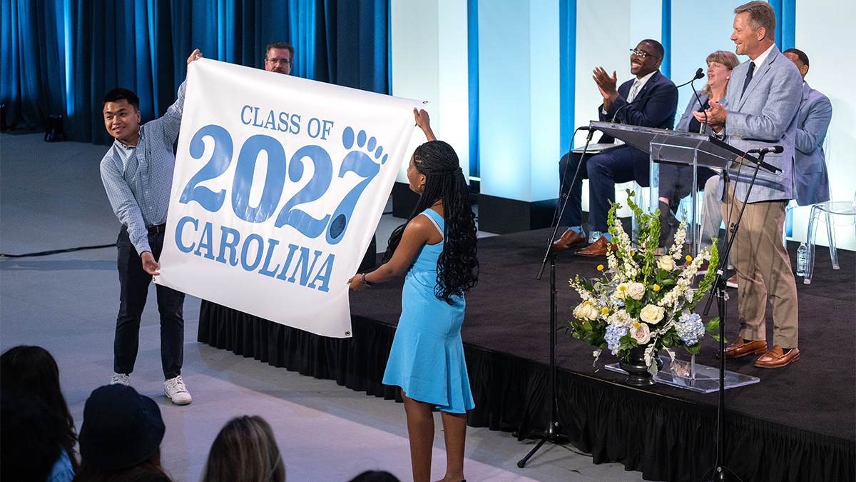 Two students unveiling a banner that reads 