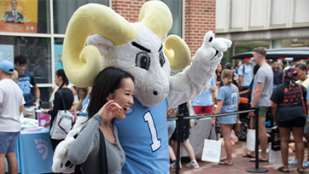 A student posing for a photo with UNC-Chapel Hill's ram mascot, Rameses.