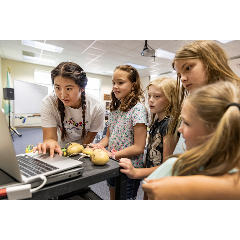 A student named Fiona Chen showing four young girls how to make potato batteries as the five of them look at a laptop.