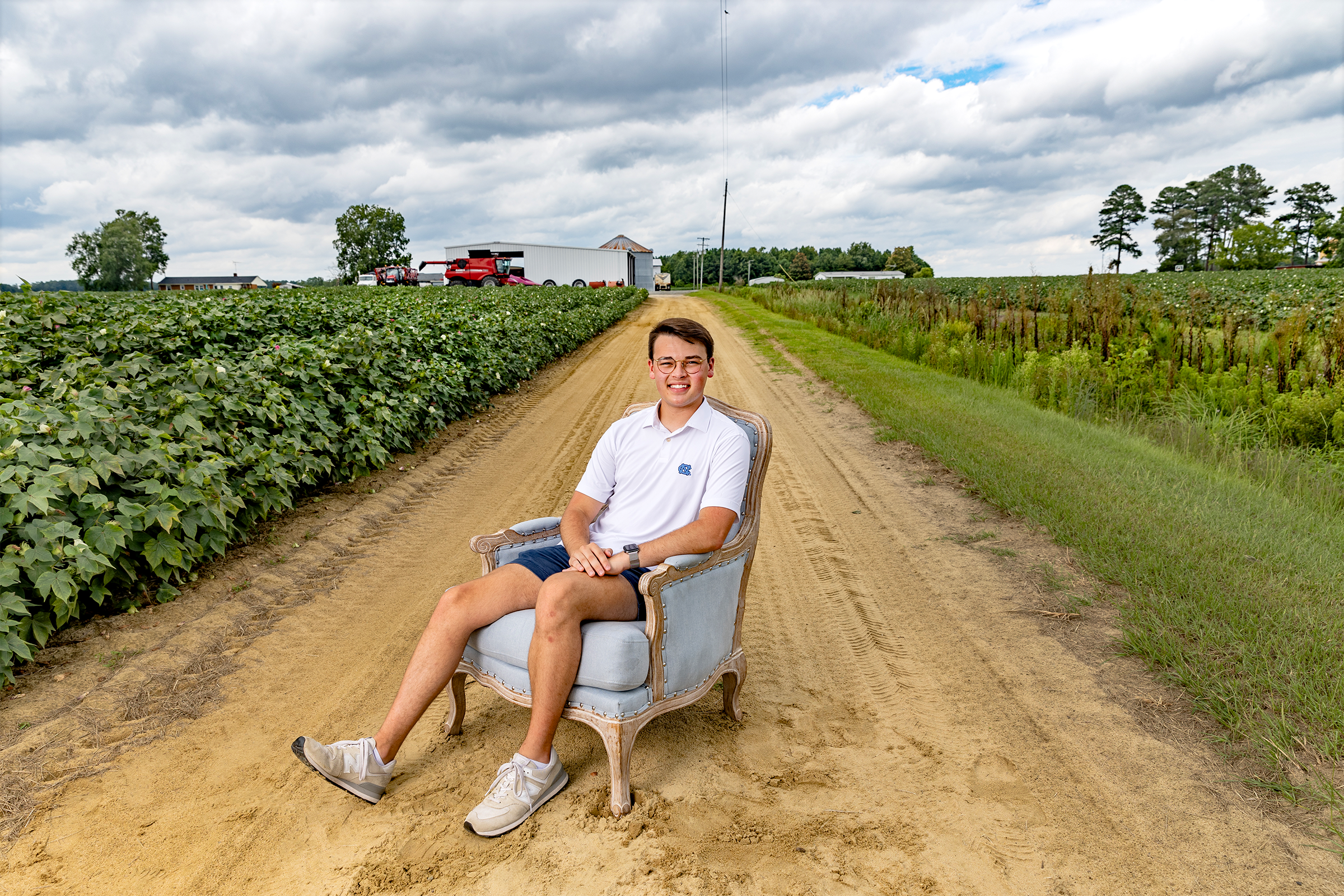 A man named Haygen Warren sitting in a blue chair and posing for a portrait on a dirt road on a farm.
