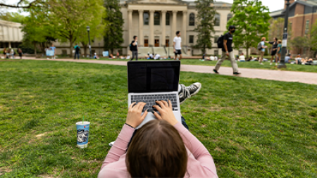 A student sitting on the lawn of Polk Place using a laptop.
