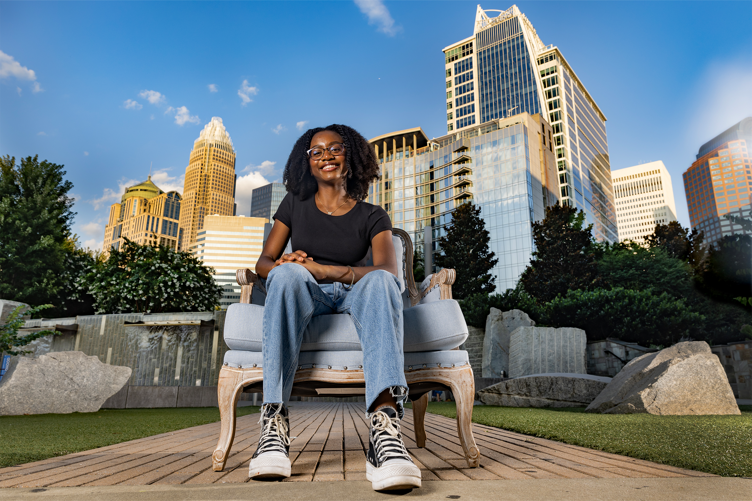 A woman named Chi-Chi Okoye sitting in a blue chair and posing for a portrait at a park in downtown Charlotte.