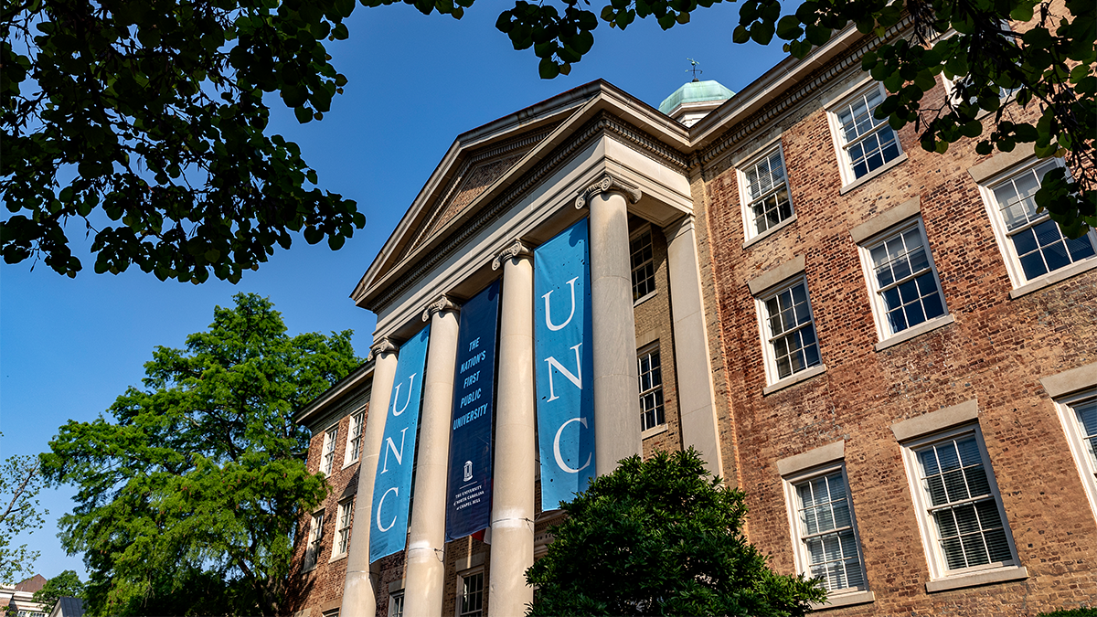 Exterior view of South Building on the campus of UNC-Chapel Hill. Three banners hang, reading: 
