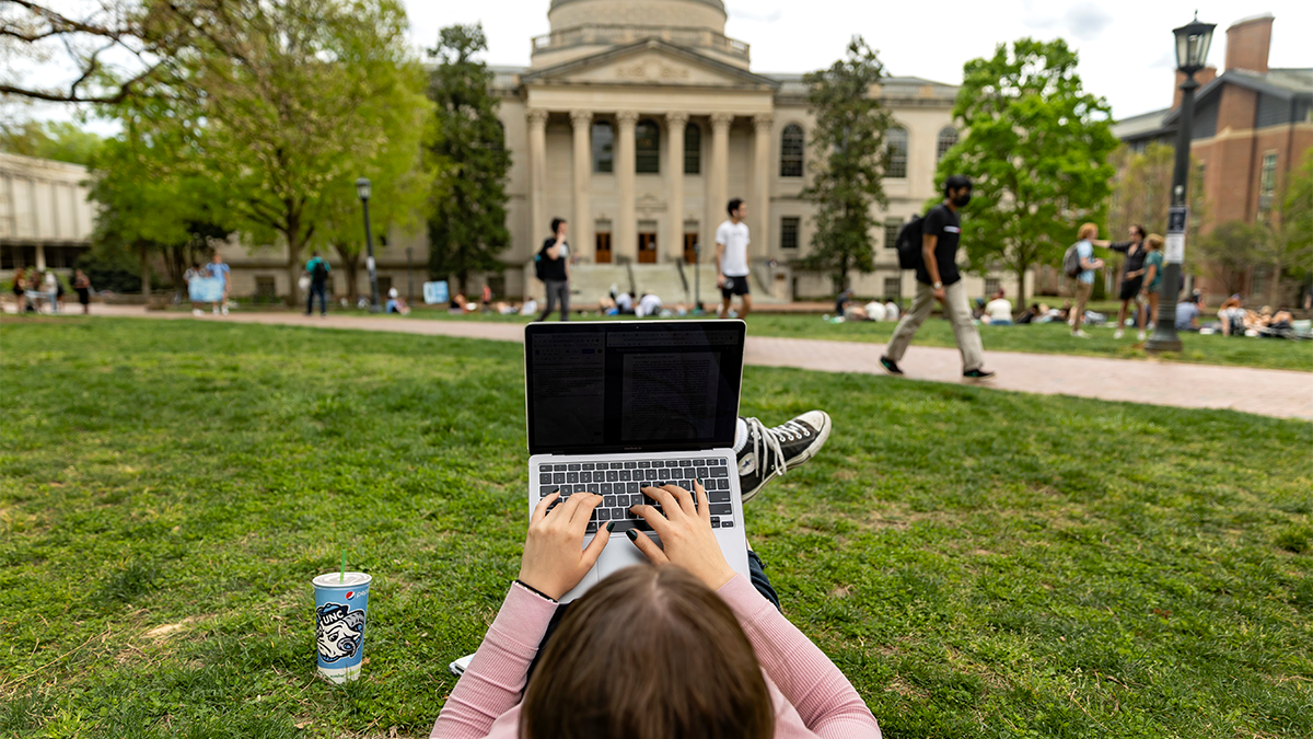 A student sitting on the lawn of Polk Place using a laptop.