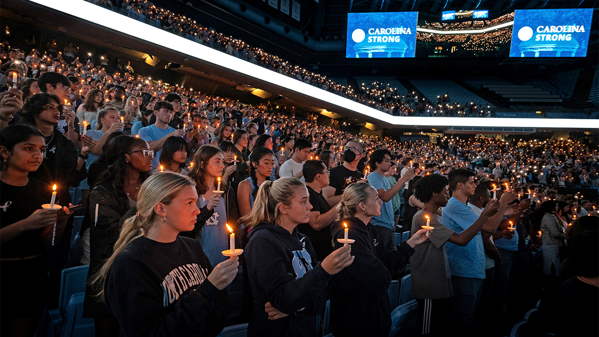 A large group of students, faculty, staff and community members standing in the Dean E. Smith Center holding candles.