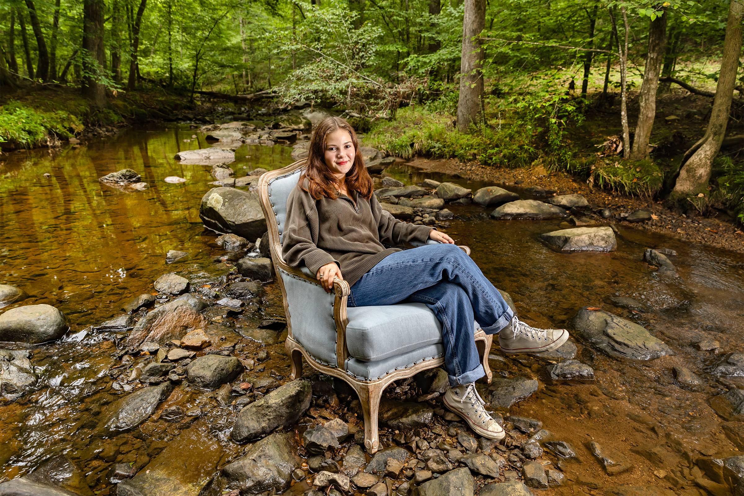 A woman named Sophie Wiss sitting in a blue chair and posing for a portrait in a creek.