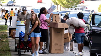 Students collecting items from cars and transporting move-in materials on a sidewalk.