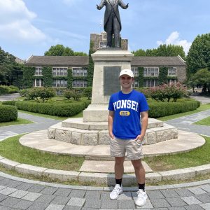A man named Ethan Delves posing for a photo in front of a statue.