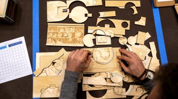 Overhead photo of a pair of hands working with pieces of wood cutouts.