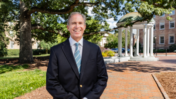 A man, John Preyer, posing for a photo in front of the Old Well on the campus of UNC-Chapel Hill.