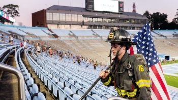 A firefighter holding an American flag and running up stadium steps.