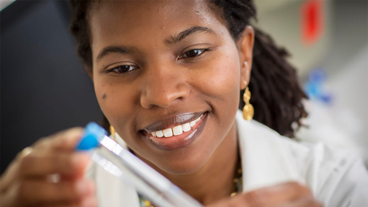 Woman smiles while examining test tube equipment.