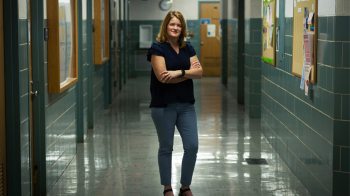 Woman stands with her arms crossed in school hallway.