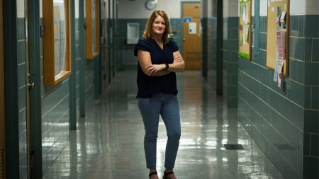 Woman stands with her arms crossed in school hallway.