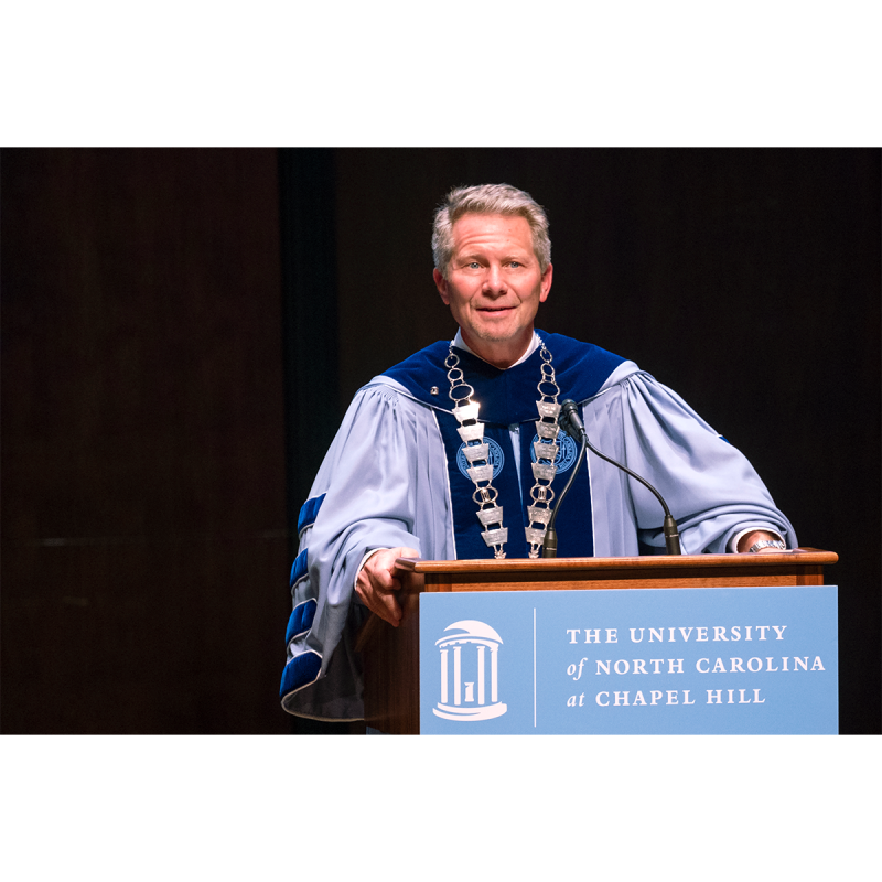 Chancellor Kevin M. Guskiewicz in regalia speaking at a podium indoors during a University Day event.