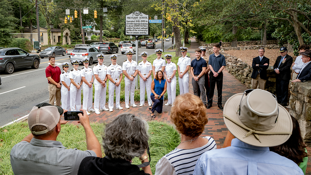 A large group of people, most of whom are Navy ROTC members dressed in white uniforms, posing for a photo in front of a newly unveiled historical marker on the side of Franklin Street.