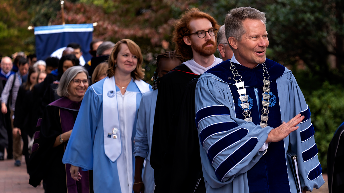 A group of people, including Chancellor Kevin M. Guskiewicz, in regalia walking around the campus of UNC-Chapel Hill during its University Day ceremony