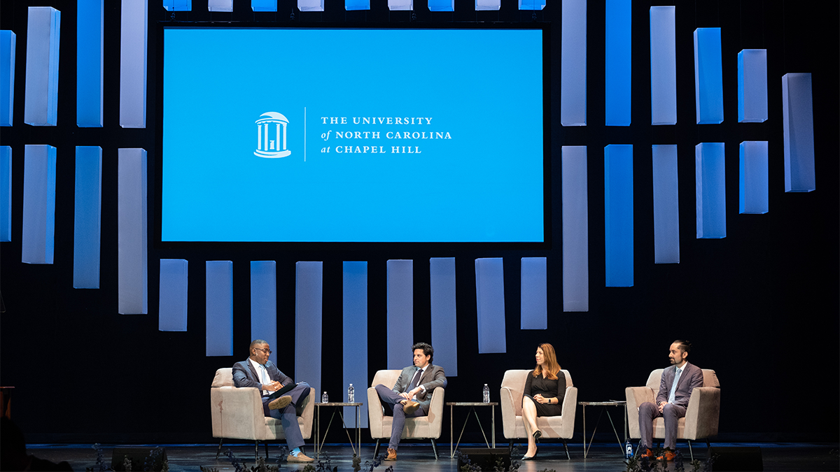 Four people sitting in chairs on a stage for a panel discussion during a University Day event.