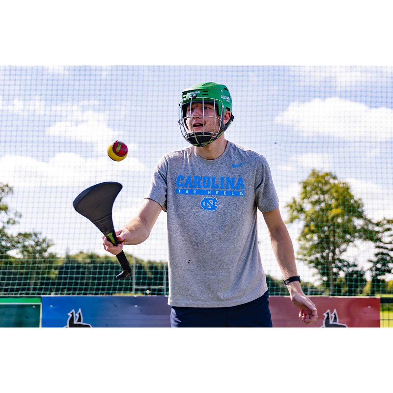 A student, Christian Jahneo, wearing a helmet and playing the Irish sport hurling.