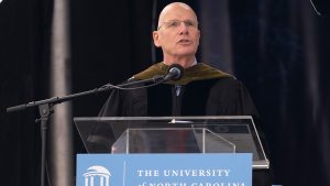 Bob Blouin wearing commencement robes speaking at a podium that reads 