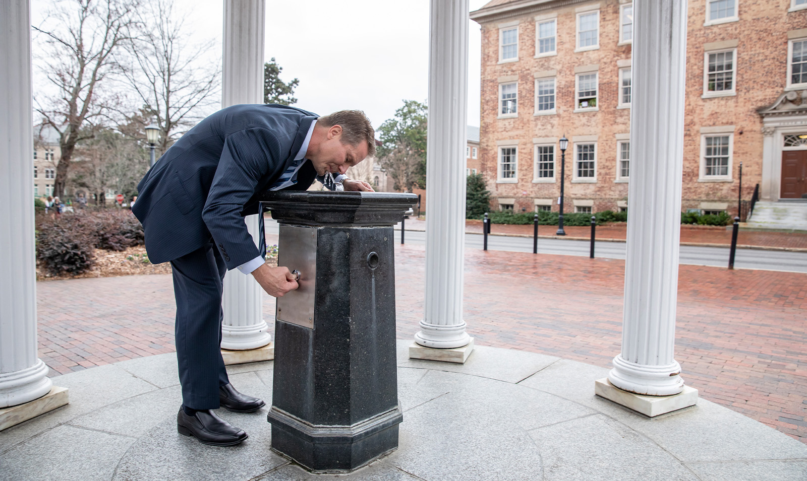 Chancellor Kevin M. Guskiewicz drinking from the Old Well on the campus of UNC-Chapel Hill on a gray, dreary February day.