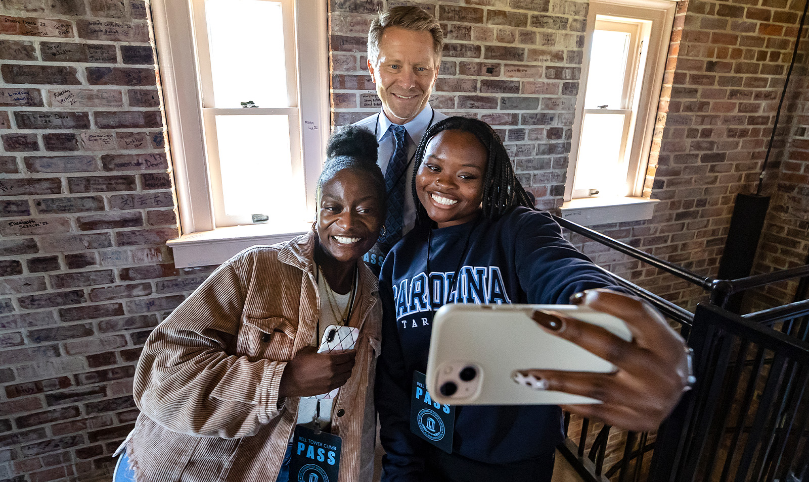 Two students taking a selfie with Chancellor Kevin M. Guskiewicz in the interior of the Morehead-Patterson Bell Tower on the campsu of UNC-Chapel Hill.