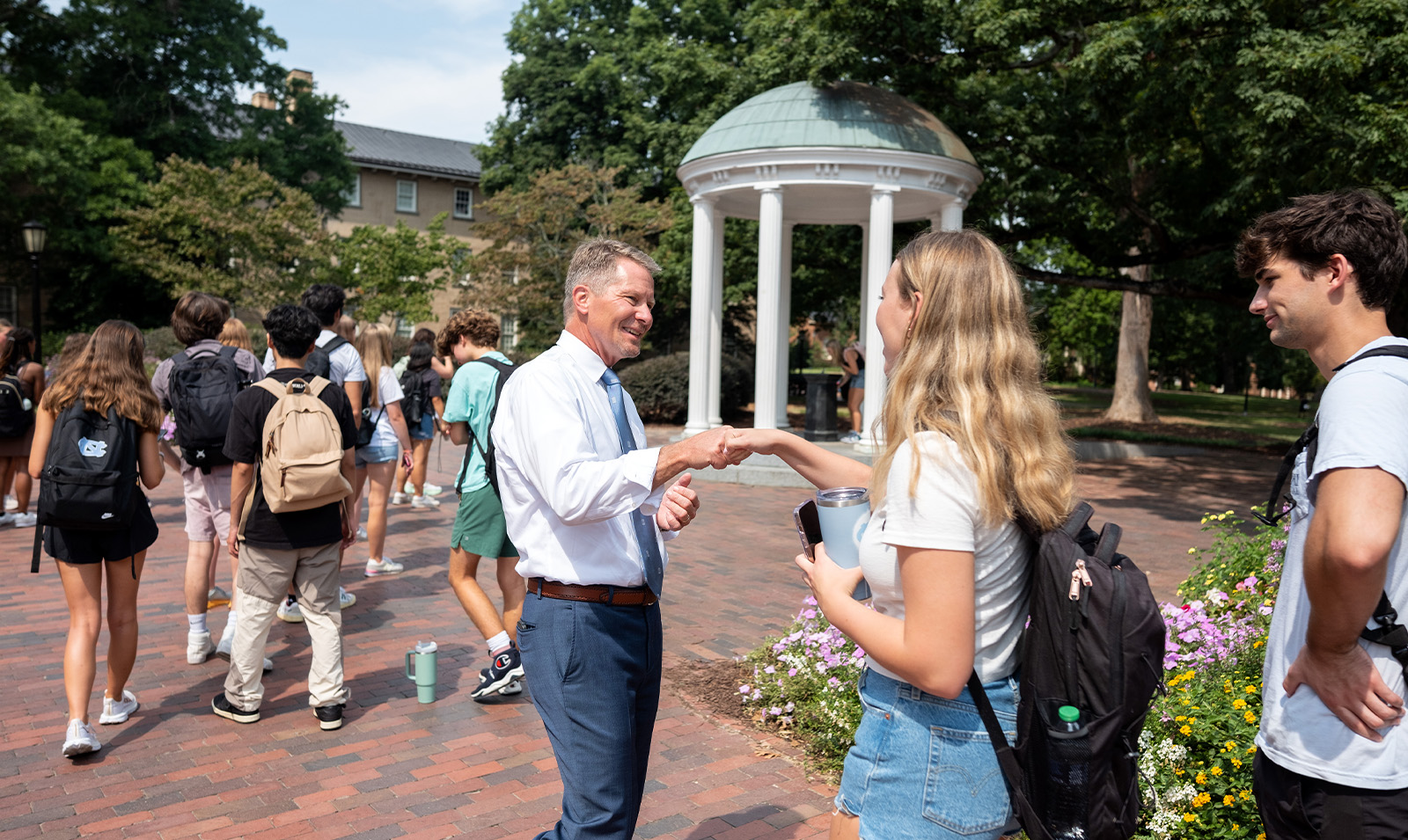 Chancellor Kevin M. Guskiewicz giving a student a fist bump as she waits in line to drink from the Old Well on the first day of the fall semester on the campus of UNC-Chapel Hill.
