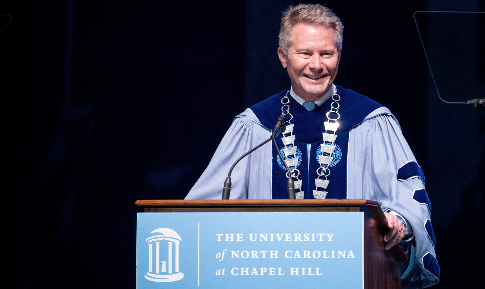 Chancellor Kevin M. Guskiewicz smiling while wearing regalia and speaking at a podium at UNC-Chapel Hill's University Day.
