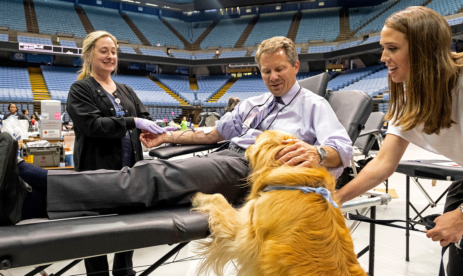 Chancellor Kevin M. Guskiewicz petting a dog while giving blood in the Dean E. Smith Center on the campus of UNC-Chapel Hill.
