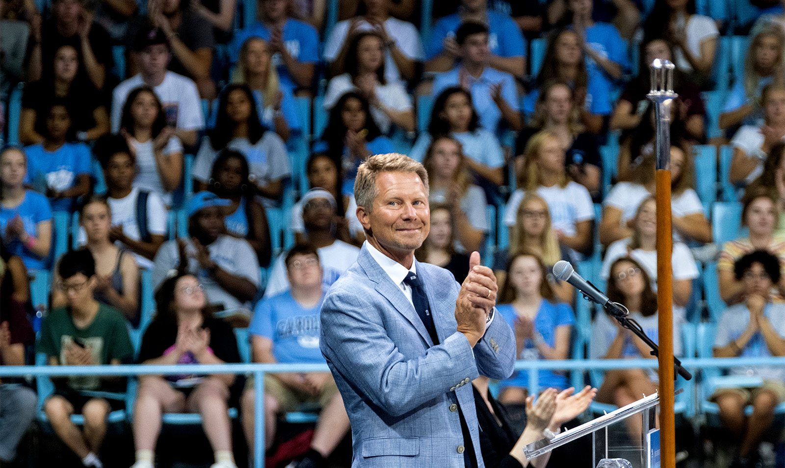 Chancellor Kevin M. Guskiewicz clapping while standing at a podium in Carmichael Arena on the campus of UNC-Chapel Hill during Convocation.