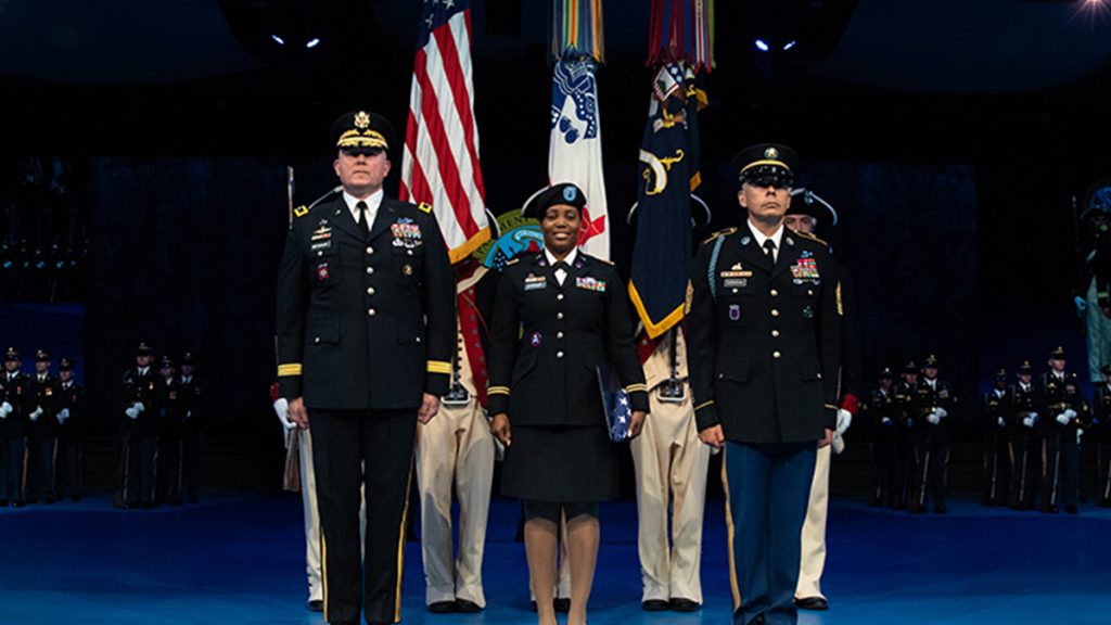 Sheree Stewart on stage standing next to two distinguished military individuals in full regalia.