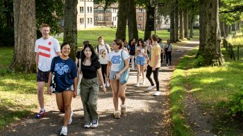 Students walking and talking as a group on a path on a shaded campus.