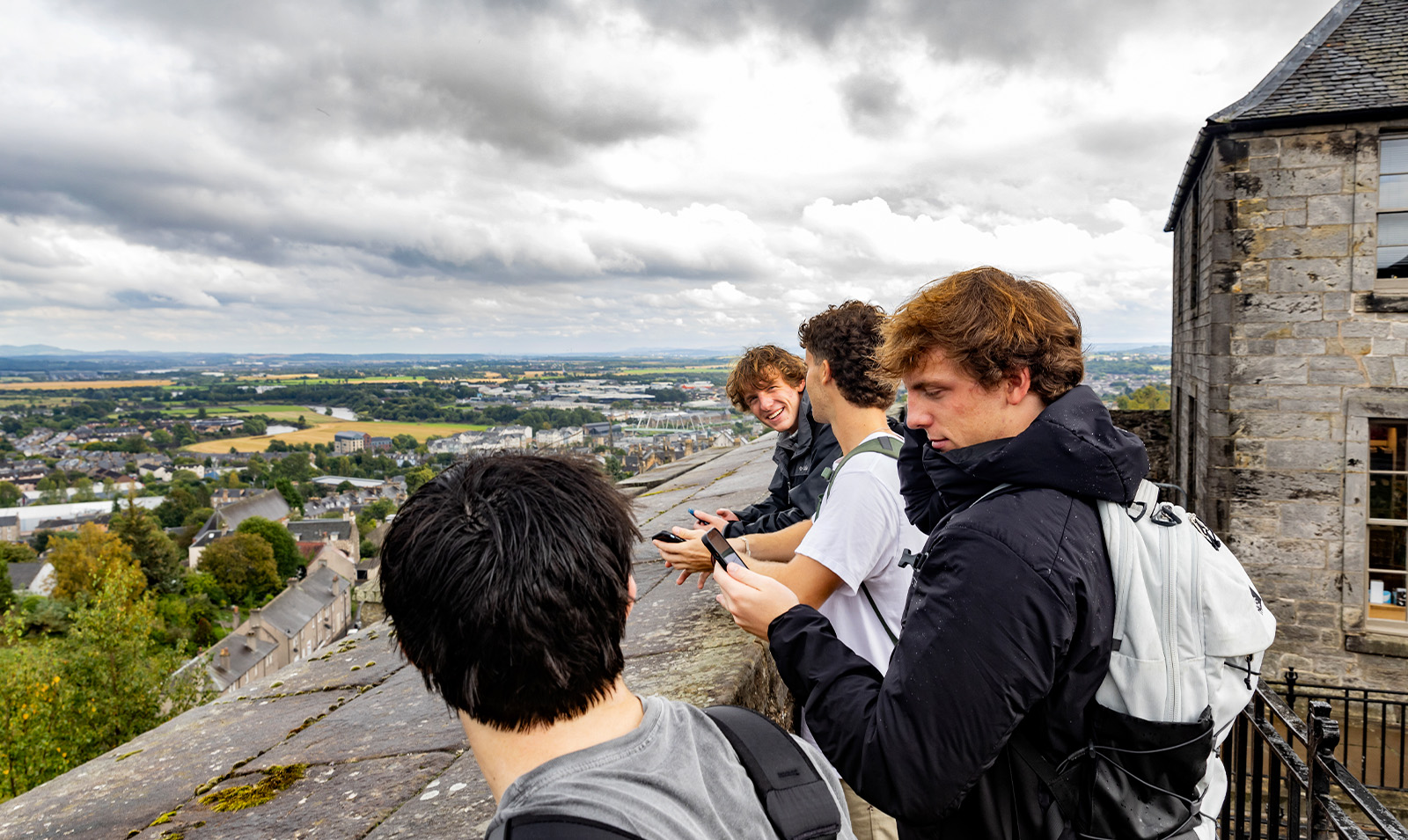 Students standing up against a wall at a high elevation and looking out at the cityscape below in Stirling, Scotland.