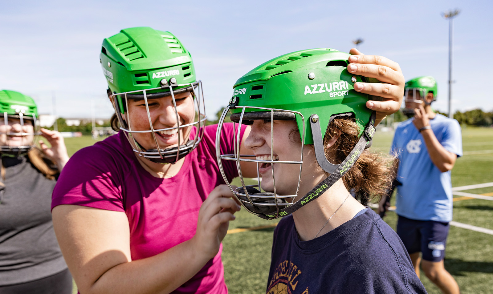 A student helping another student put on her helmet before practicing a sport called hurling.