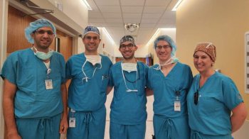 Five doctors wearing scrubs pose arm in arm.